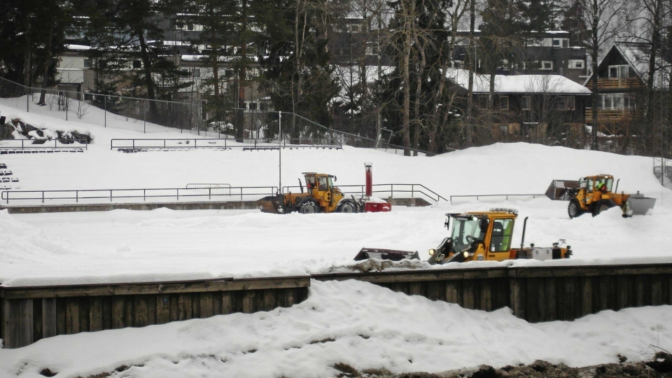 HER JOBBES DET: Kommunens arbeidere jobber hardt for å få snøen fjernet og banen klar til seriestart.