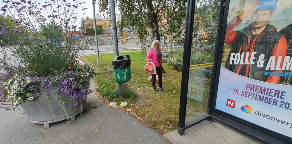 BLOMSTER VS. SØPPEL: Foran den overfylte søppeldunken har kommunen satt opp en stor blomsterurne med flotte blomster, men det er søppelet som sjenerer Berit Kaarbø og flere andre innbyggere vi har snakket med. Foto: Yana Stubberudlien